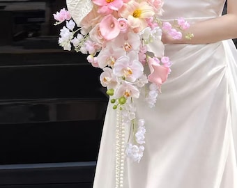 May include: A cascading bridal bouquet featuring a mix of pink and white flowers, including orchids, calla lilies, and anthuriums, accented with delicate white pearl strands that drape downward from the floral arrangement.