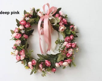 May include: A pink floral wreath with a pink ribbon bow. The wreath is made of artificial flowers and greenery.