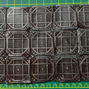 Può includere: Primo piano di un foglio di 18 piastrelle quadrate, ciascuna con un design geometrico argento e marrone. Le piastrelle sono disposte in un motivo a griglia.