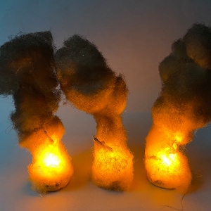 Puede incluir: Tres objetos redondos, esponjosos y de color marrón claro con una luz naranja incandescente en su interior. Los objetos están dispuestos en fila sobre una superficie blanca.