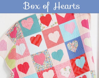 May include: A patchwork quilt with a heart design. The quilt features squares in various colors, including red, pink, and blue, each with a heart in the center. The text "Box of Hearts" is at the top. The quilt is a crib size and is a fat quarter pattern in 4 sizes.