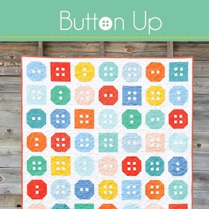 May include: A colorful quilt with a button design, featuring red, orange, yellow, green, and blue squares and octagons on a white background. The quilt is hanging against a wooden wall. The text "Button Up" is at the top.