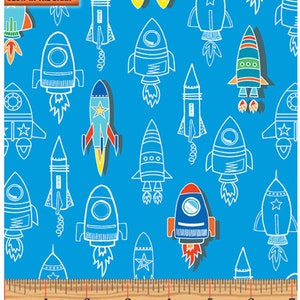 May include: A blue fabric with a repeating pattern of white outlined rockets. The rockets are in various styles and colors, including red, yellow, green, and blue. The fabric has the words "Glow in the Dark" printed in the top left corner.