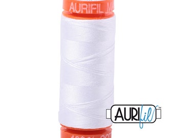 May include: A white spool of Aurifil thread with orange labels. The label reads "Aurifil 50 wt Cotton 100% Cot" and "Aurifil".