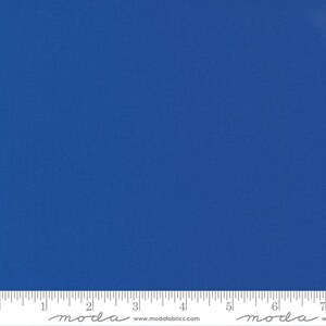 May include: A close-up of a vibrant blue fabric with a subtle textured pattern. A ruler is placed at the bottom of the fabric, with measurements in inches. The fabric is a solid color, with no other patterns or designs.