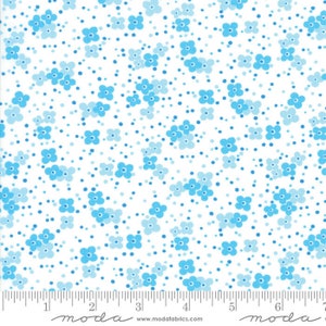 May include: White fabric with a repeating pattern of small blue flowers and tiny blue dots. The fabric has a ruler at the bottom with the word "moda" printed on it.