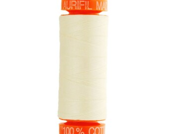 May include: A spool of Aurifil thread in a light cream color. The spool is labeled "Aurifil Made in USA" and "100% Cotton".