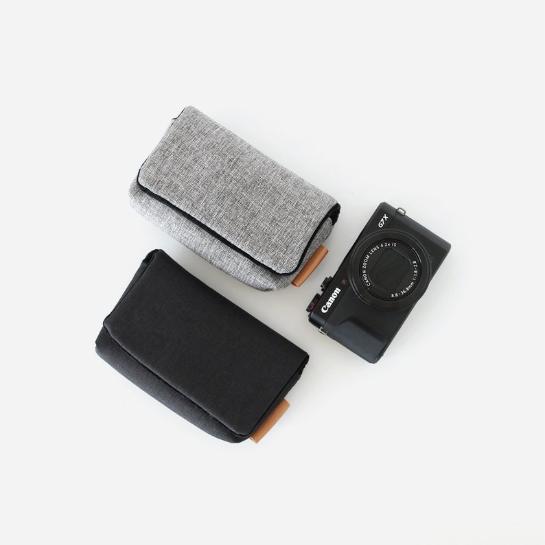 May include: Two camera cases, one gray and one black, with a black Canon G7X camera on a white background.