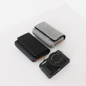 May include: Two camera cases, one gray and one black, with a black Canon camera with a lens that says "Canon Zoom Lens 4.2-12.6 1:3.8-6.3 28-100mm" on it.