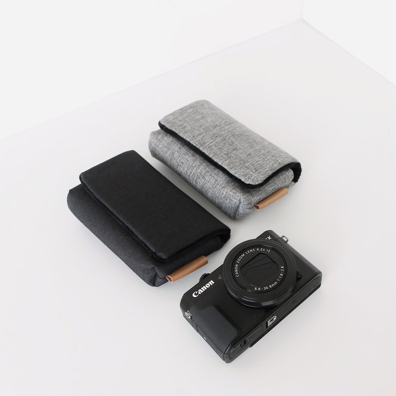 May include: Two camera cases, one gray and one black, with a black Canon camera with a lens that says "Canon Zoom Lens 4.2-12.6 1:3.8-6.3 28-100mm" on it.