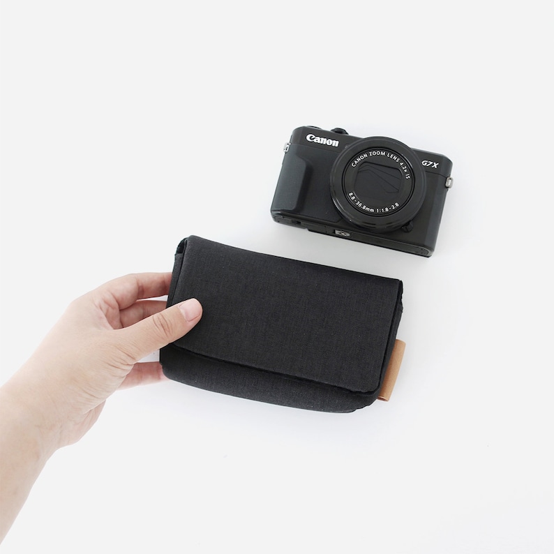 May include: A black Canon PowerShot G7 X Mark II camera with a black camera case. The camera case has a brown leather pull tab.