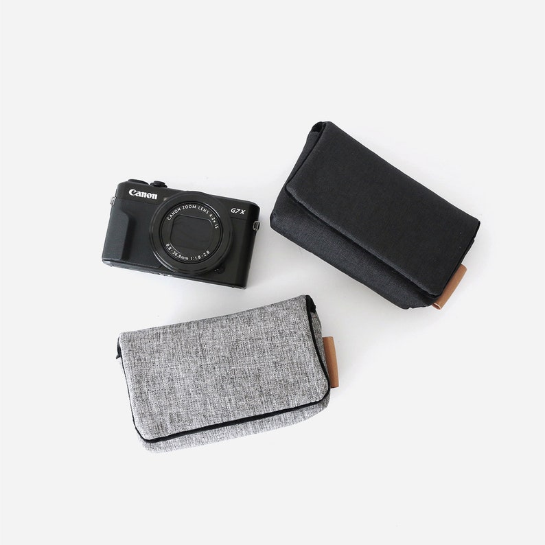 May include: Two camera cases, one black and one gray, with a black Canon G7X camera in the center.