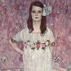 Op de afbeelding: Een jong meisje in een witte jurk met een bloemenrand staat tegen een roze achtergrond met witte bloemen. Ze heeft lang donker haar en draagt een blauwe strik in haar haar.