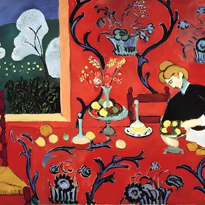 May include: A woman sits at a table with a red tablecloth featuring a floral pattern. The table is laid with a bowl of fruit, a vase of flowers, and a bottle of wine. The woman is wearing a black dress and a white apron. The background is a red wall with a floral design.