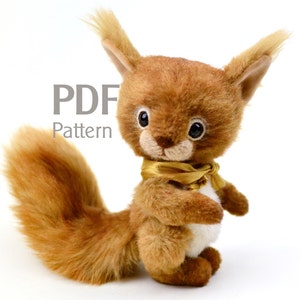 Puede incluir: Patrón PDF para un juguete de peluche de ardilla. La ardilla es marrón con una cola esponjosa y lleva una cinta dorada alrededor del cuello. El patrón está disponible para descargar.