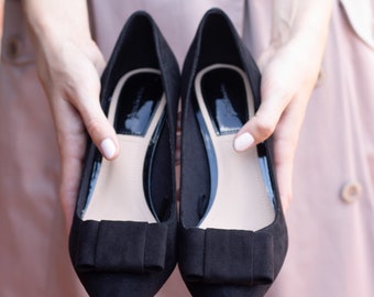 May include: A pair of black suede flats with a bow detail on the toe.