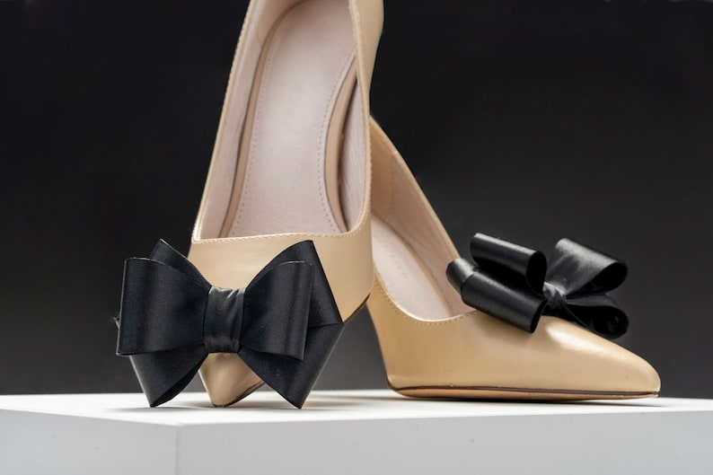 Pode incluir: Um par de sapatos de salto alto bege com la&ccedil;os de cetim preto nos dedos.