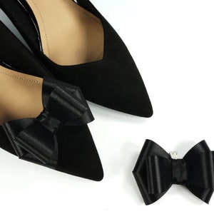 Pode incluir: Dois sapatos de cetim preto com la&ccedil;os de cetim preto nos dedos. Tamb&eacute;m &eacute; mostrado um la&ccedil;o de cetim preto separado.