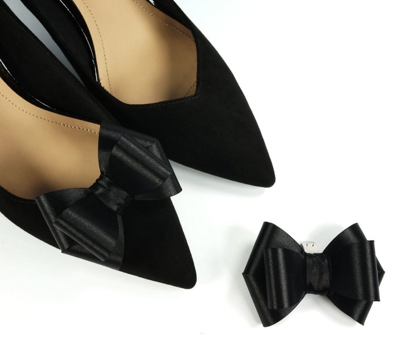 Pode incluir: Dois sapatos de cetim preto com la&ccedil;os de cetim preto nos dedos. Tamb&eacute;m &eacute; mostrado um la&ccedil;o de cetim preto separado.