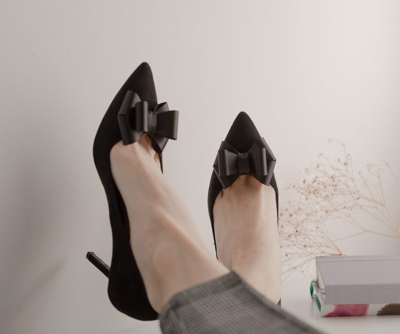 Pode incluir: Um par de sapatos pretos de salto alto com la&ccedil;os de cetim preto nos dedos.