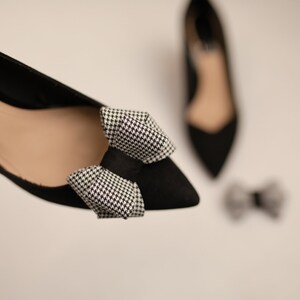 May include: A pair of black pointed-toe heels with a black and white houndstooth bow on the toe.