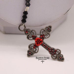 May include: A black beaded necklace with a silver filigree cross pendant adorned with red rhinestones and a red rose. The pendant features the text "Blood & Stars Jewellery".