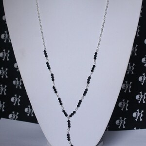 May include: A silver chain necklace with black beads and a silver filigree cross pendant. The necklace is displayed on a white mannequin bust against a black and white skull pattern background. The text "BLOOD & STARS JEWELLERY" is visible at the top of the image.