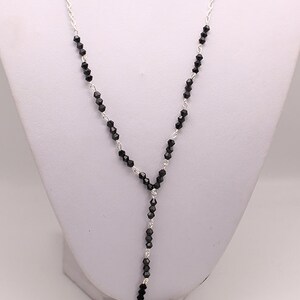 May include: A silver chain necklace with black beads and a silver cross pendant with red crystals. The cross has a detailed design and is accented with black crystals.