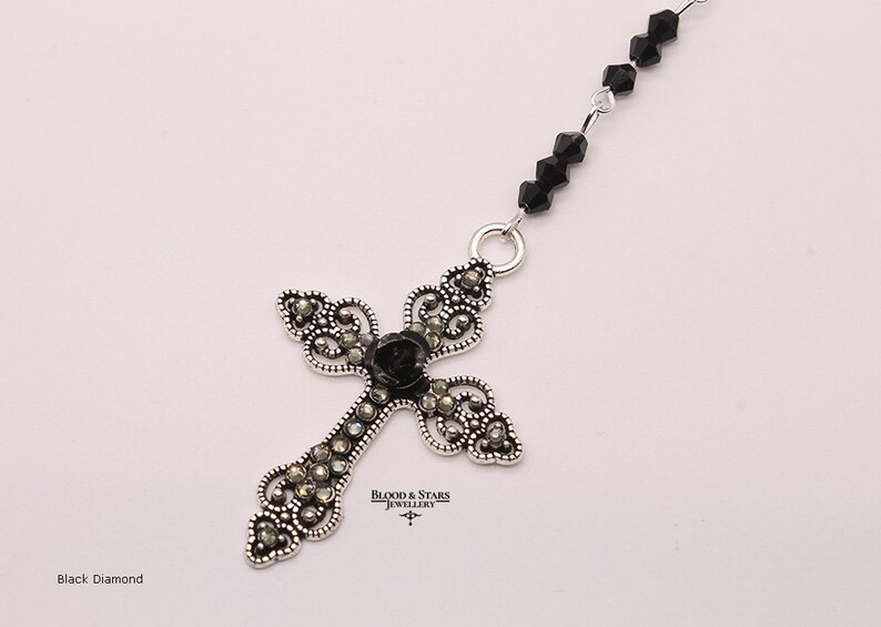 May include: A silver cross pendant with black diamond accents and a black rose in the center. The cross is attached to a black beaded chain.