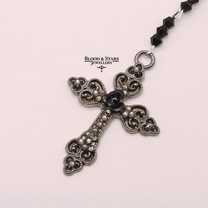 May include: A silver filigree cross pendant with a black diamond center, hanging from a black beaded chain.  Blood & Stars Jewellery.