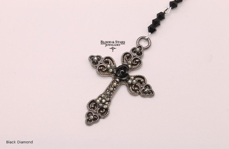 May include: A silver filigree cross pendant with a black diamond center, hanging from a black beaded chain.  Blood & Stars Jewellery.