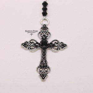 May include: A silver filigree cross pendant with black crystal accents. The cross is attached to a black beaded chain.