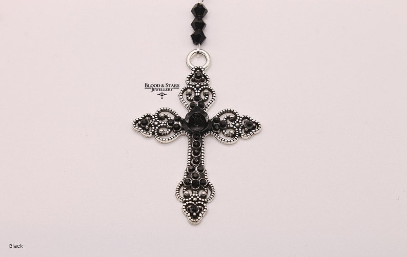 May include: A silver filigree cross pendant with black crystal accents. The cross is attached to a black beaded chain.