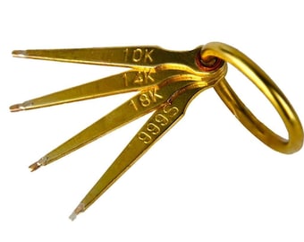 May include: A set of gold-colored metal jewelry testing tools attached to a ring. Each tool is labeled with a karat marking: 10K, 14K, 18K, and 999S. The tools are designed for testing the purity of gold.