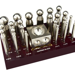 Könnte beinhalten: Ein Satz Metallwerkzeuge zur Schmuckherstellung, darunter Prägestempel und ein Prägeblock, angeordnet in einem dunklen Holzhalter. Die Werkzeuge sind in verschiedenen Größen und Formen erhältlich, mit Messungen in mm. Der Block ist mit "DAPPING BLOCK" beschriftet.