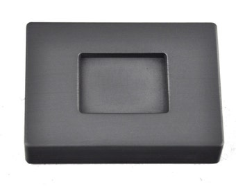 May include: A gray rectangular mold with a square opening in the center. The mold is used for casting metal.