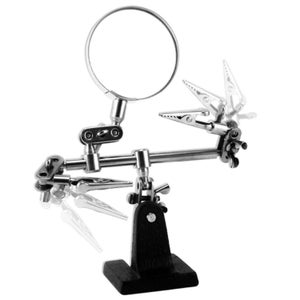 May include: A silver-colored helping hands tool with a magnifying glass and two alligator clips. The tool is mounted on a black base and is designed to hold small objects for soldering or other detailed work.