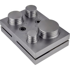 May include: A metal punch set with four different sized circular punches. The punches are arranged in a rectangular metal base with a silver finish. The base has markings for 1/2", 1", 1 1/2", and 2" punches.