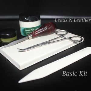 May include: A leatherworking basic kit with a white tile, a small jar of leather conditioner, a small jar of leather dye, a leather stitching awl, a pair of tweezers, and a leather burnishing tool. The kit is labeled "Leads N Leather" and "Basic Kit".