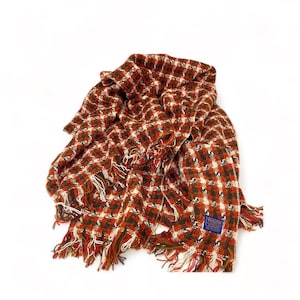 May include: A brown, red, and white checkered throw blanket with fringe. The blanket is made of wool and has a label that says "Premier Wools".