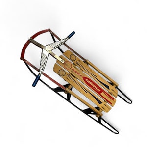 May include: A vintage wooden sled with a red and black metal frame. The sled has a Champion brand label and a Gladding label. The sled has a metal steering mechanism with blue handles.