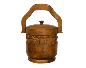 May include: A wooden ice bucket with a carved design and a handle. The bucket is brown and has a lid.