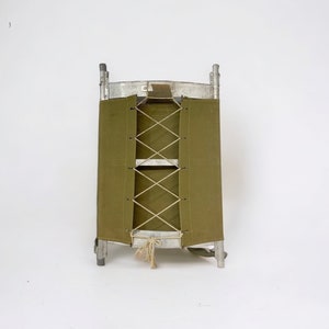 May include: A vintage green canvas cot with an aluminum frame. The cot is folded up and ready to be carried. The cot has a rope lacing system to secure the canvas.