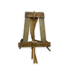 May include: A wooden easel with a canvas stretcher and a brown canvas strap. The easel is made of wood and has a green paint finish.