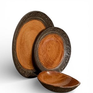 May include: A set of three ceramic serving dishes. The set includes two round plates and one oval bowl. The plates and bowl have a brown interior and a dark brown, ornate border. The plates are different sizes.