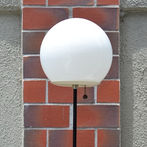 Vintage glass orb mid century atomic style floor lamp black and white with a stucco and brick wall.