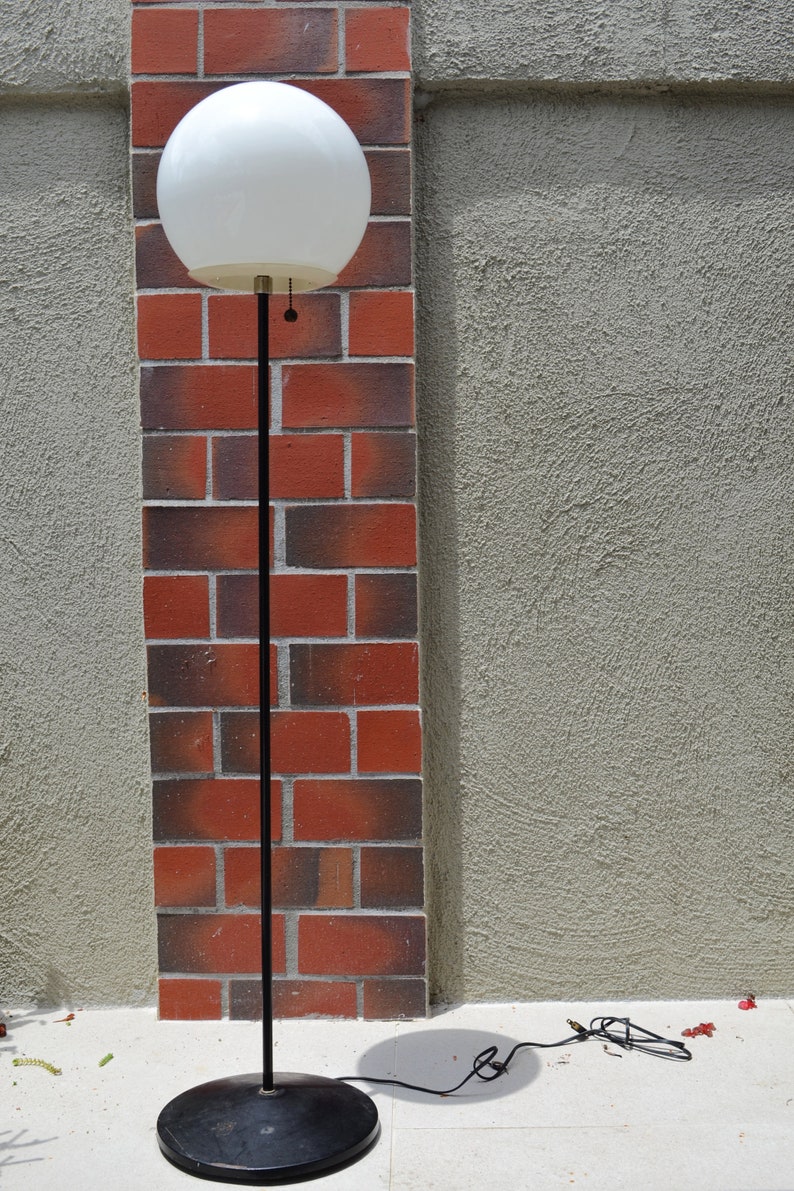 Vintage glass orb mid century atomic style floor lamp black and white with a stucco and brick wall.