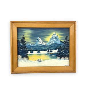 May include: A framed painting of a snowy mountain scene with a lake in the foreground. The sky is a dark blue with a yellow glow in the center. The mountains are blue and white, and the trees are green. The painting is signed "J. Swin" in the lower right corner.