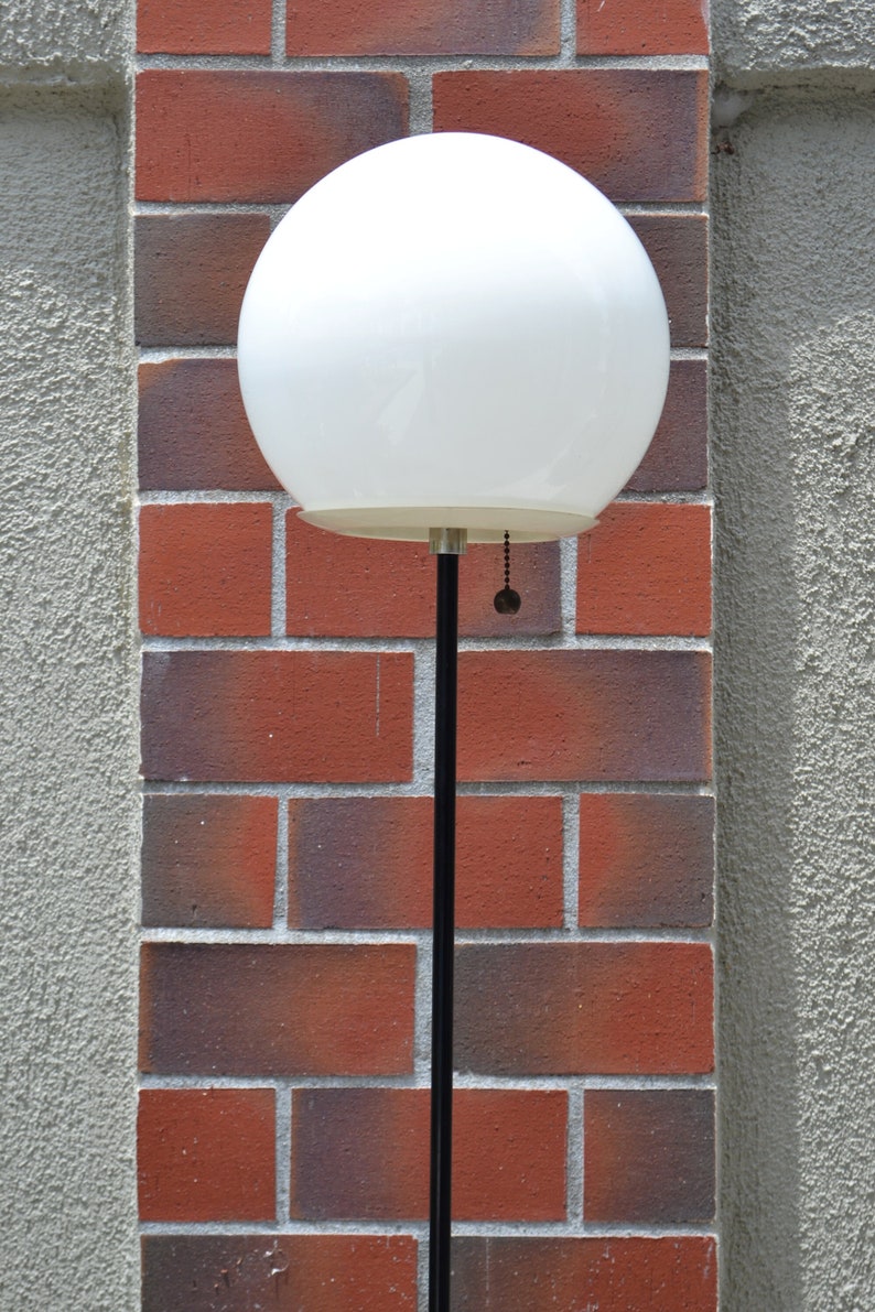 Vintage glass orb mid century atomic style floor lamp black and white with a stucco and brick wall.