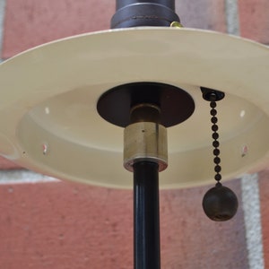 May include: A white ceiling lamp with a black metal base and a pull chain. The lamp has a round, flat shade.